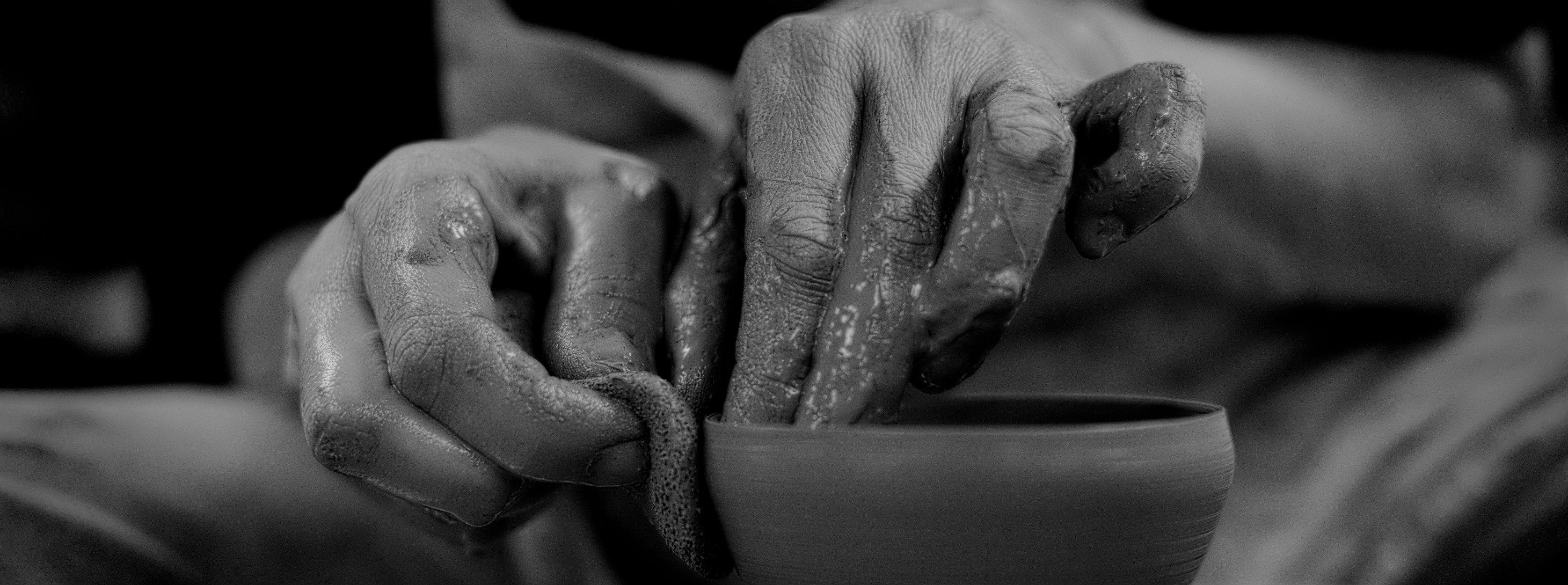 Clay-covered hands shaping a small bowl on the potter's wheel