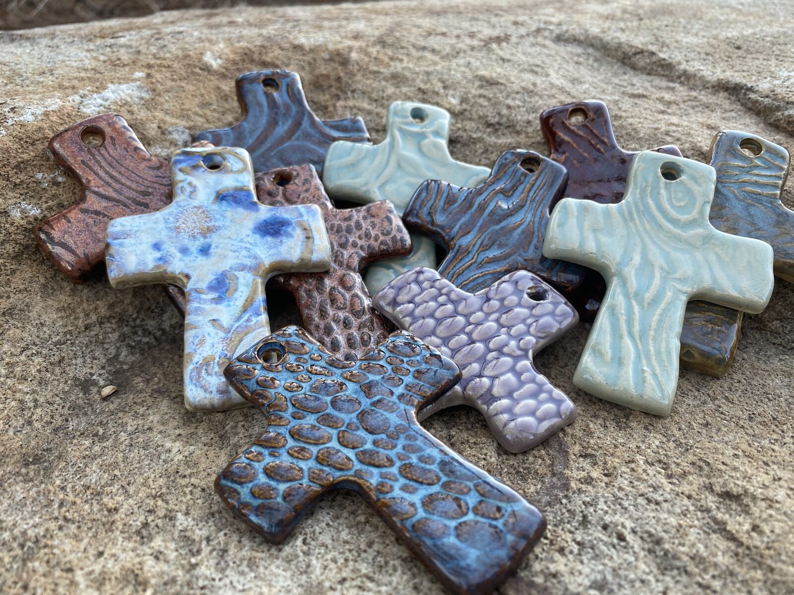 Collection of small ceramic crosses with various textures including woodgrain, pebble, and hammered patterns