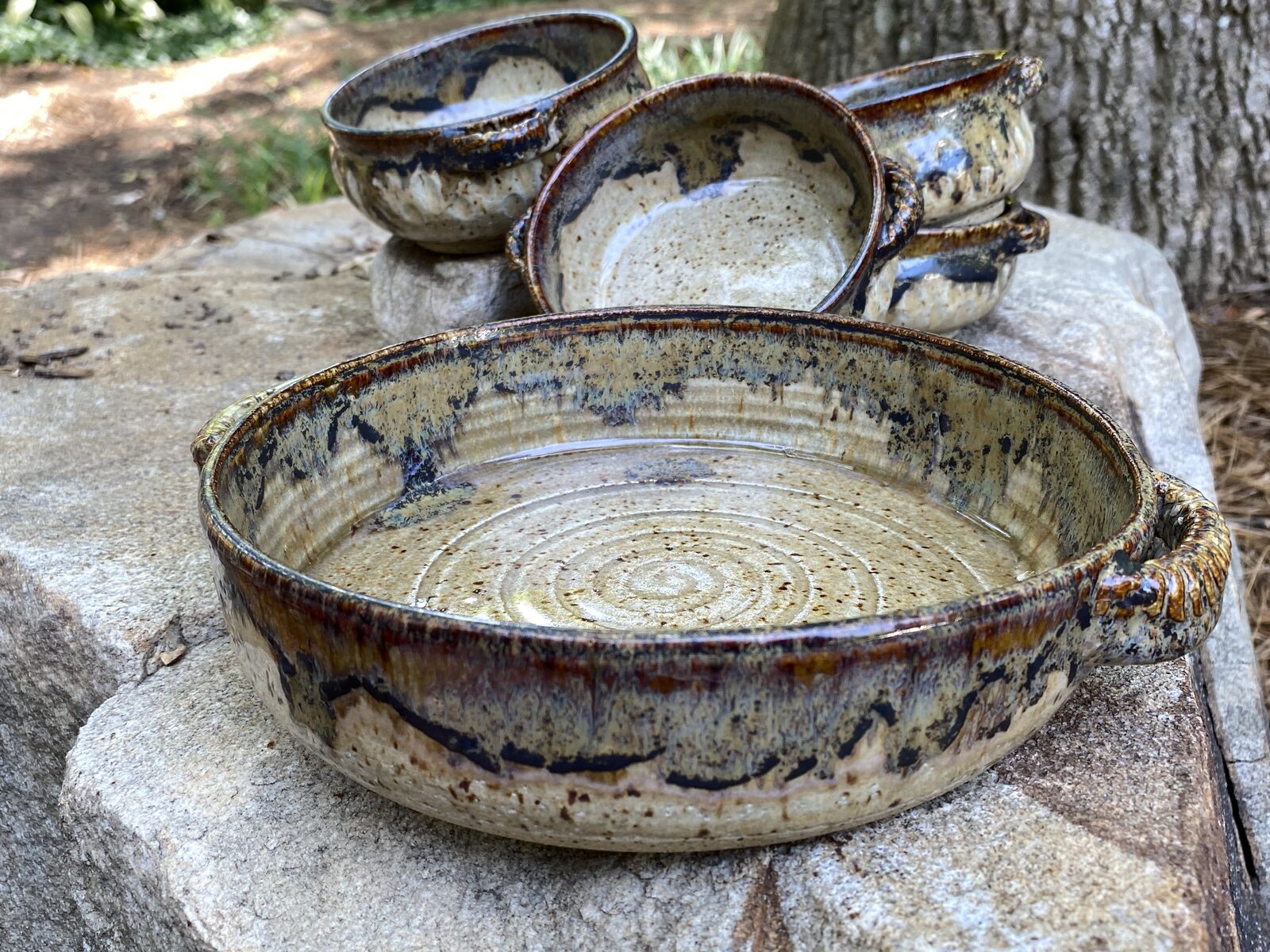 Large round handled baker with speckled cream and brown glaze, shown with matching bowls