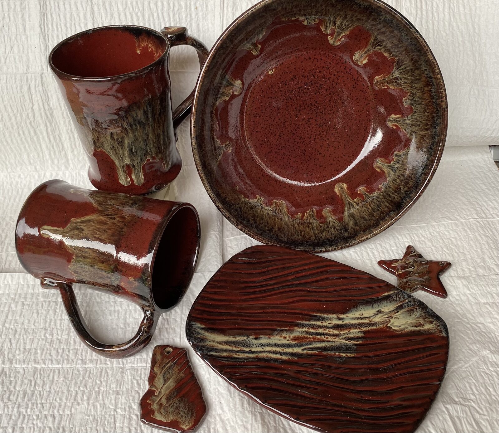 Grouping of pottery in deep red iron-rich glaze including tall mugs, a round bowl, and a textured oval platter