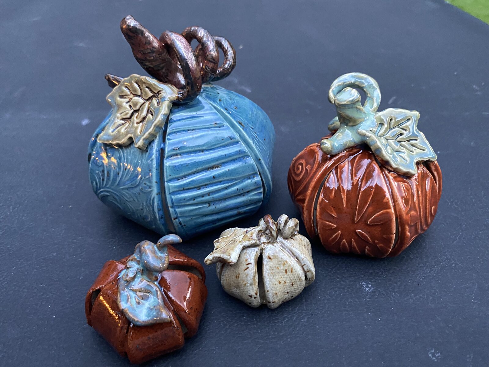 Family of ceramic pumpkins in different sizes with twisted curly stems and ceramic leaves, in blue, rust, and cream glazes