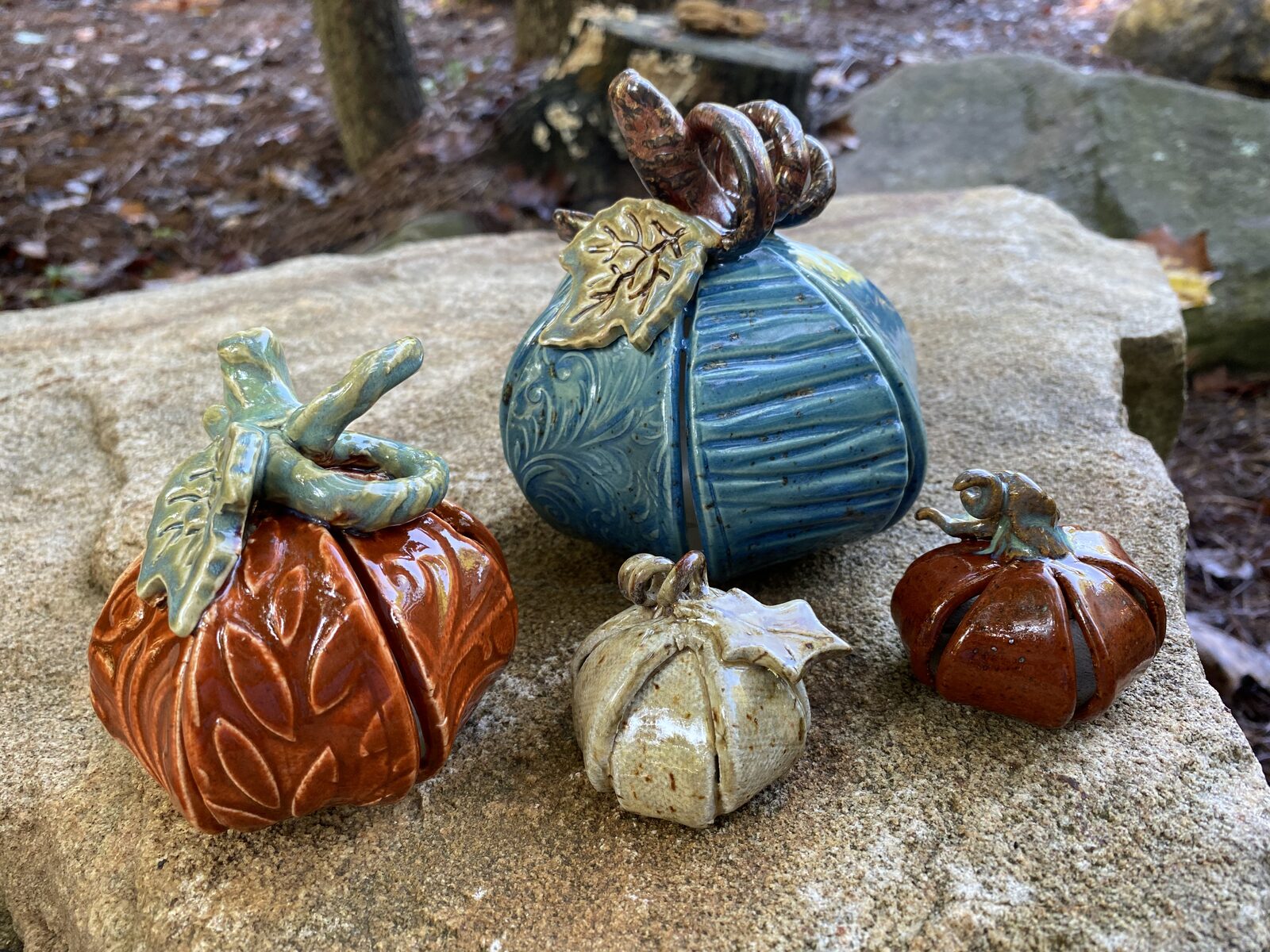 Ceramic pumpkins in autumn colors arranged on a stone outdoors, with curling vine stems and leaves
